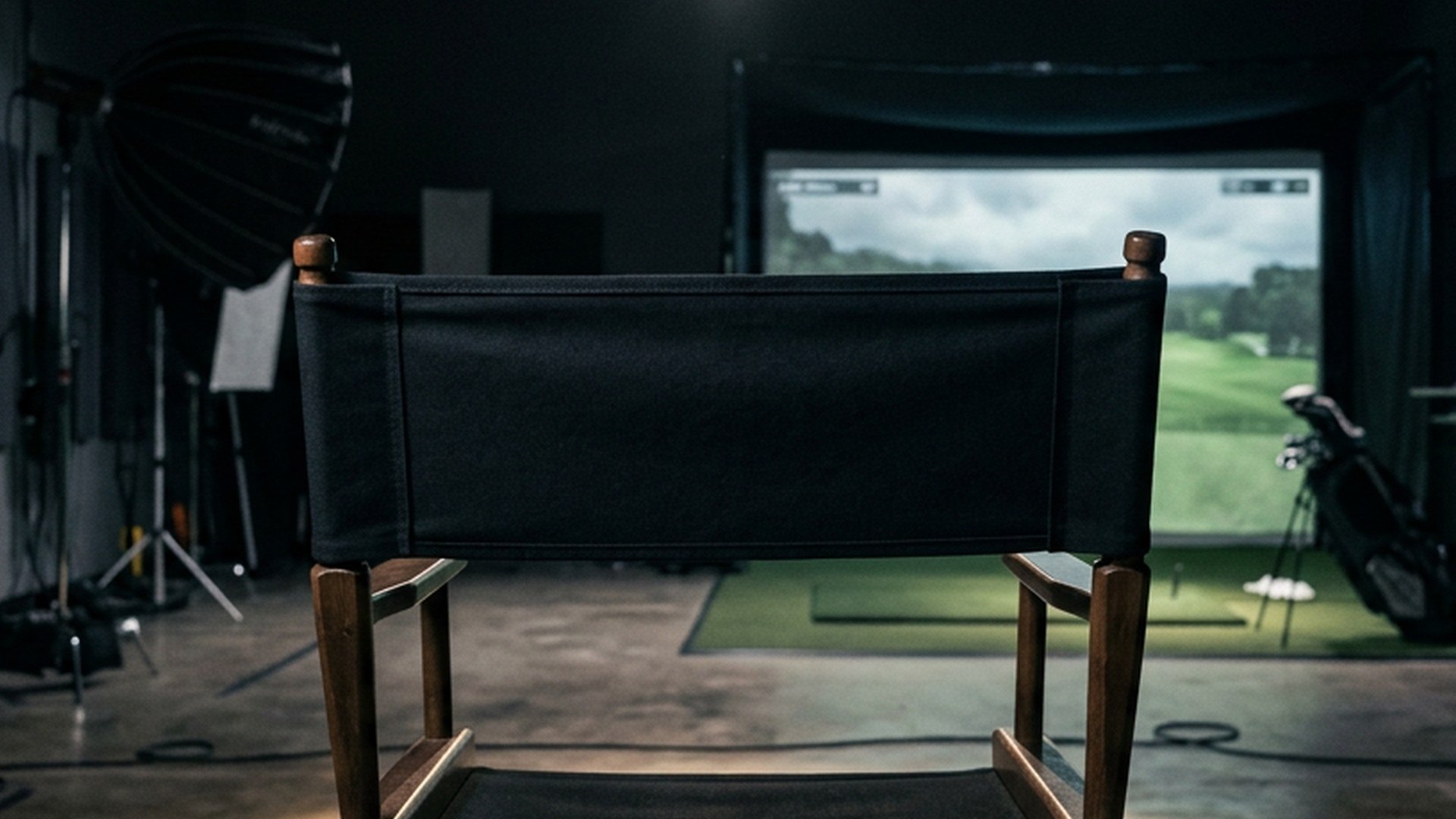 Empty director's chair spotlit from above in a dark studio with a golf simulator behind