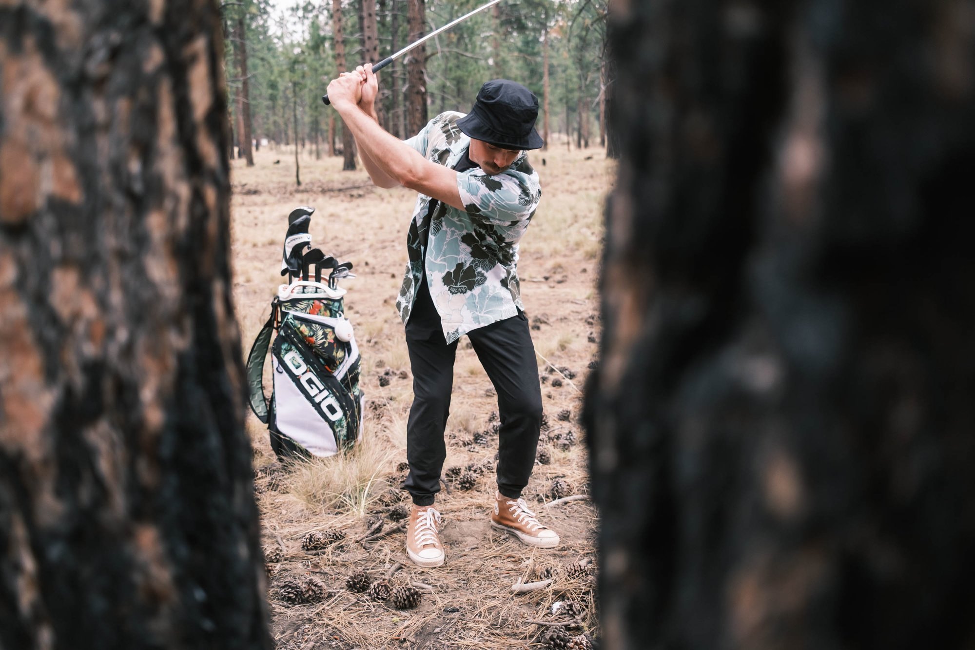 Golfer swinging between trees with OGIO bags